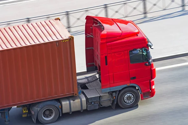 Truck with a container on a trailer rides on a city highway, close up aerial view