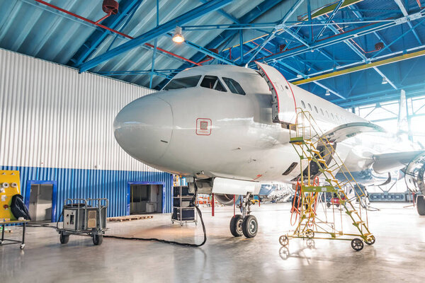 Airplanes under repair in a maintenance hangar. View of the nose and cockpit, open front door with a technical staircase