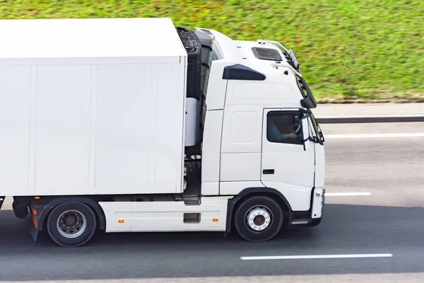 White truck with a container on a trailer rides on a city highway, side aerial view