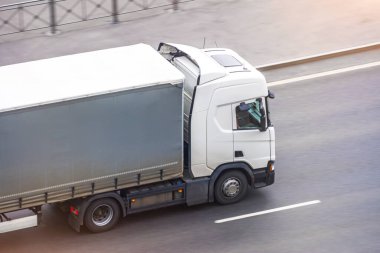 Gri tenteli beyaz kamyon şehir otobanında, yan hava manzaralı.