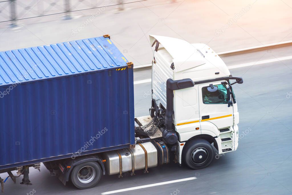 White truck with a blue container on the trailer rides on a city highway, side aerial view