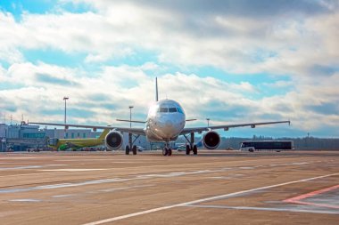 Sabah güneşiyle aydınlatılan uçak, havalimanı ve gökyüzü bulutlu arka planda iniş yaptıktan sonra pistte ilerliyor.