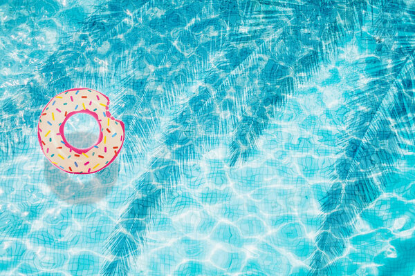 Top view of pool bottom with inflatable donut with shadow of palm