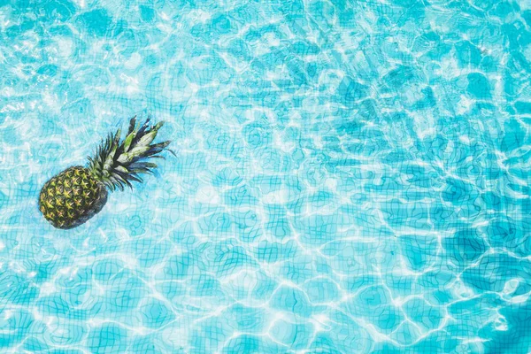 Top view of pool bottom with floating pineapple and shadow of palm