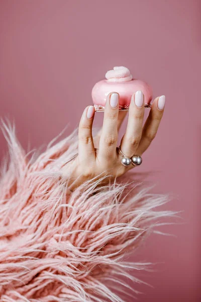 young womans hand holds a pink cake with cream in a pink coat on a pink background