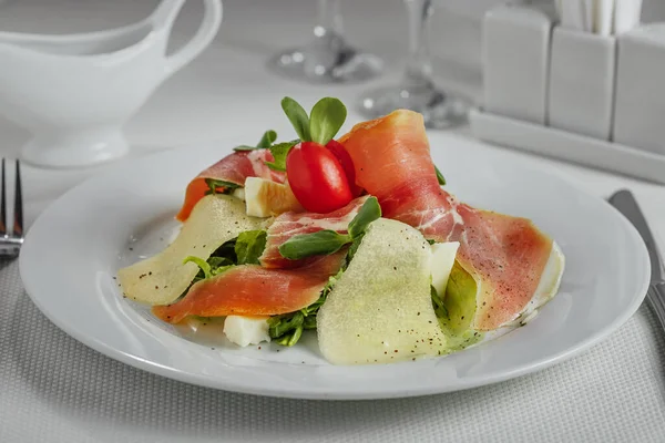 salad with prosciutto pear slices, tomatoes and herbs on a white plate, top view, top