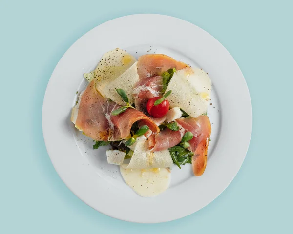 Insalata con fette di pera di prosciutto, pomodori ed erbe aromatiche su un piatto bianco, vista dall'alto, sopra — Foto Stock