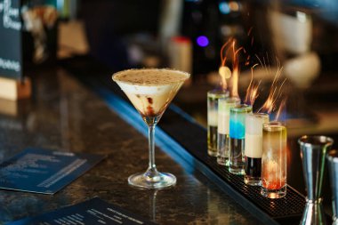 Ateşli kısa kokteylleri olan bir bar tezgahı. Martini bardağında kremalı kahve kokteyli. Bardaktaki alevler. Yanan kokteyl