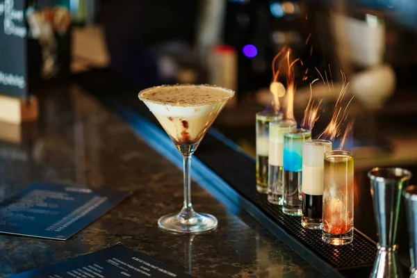 Ateşli kısa kokteylleri olan bir bar tezgahı. Martini bardağında kremalı kahve kokteyli. Bardaktaki alevler. Yanan kokteyl