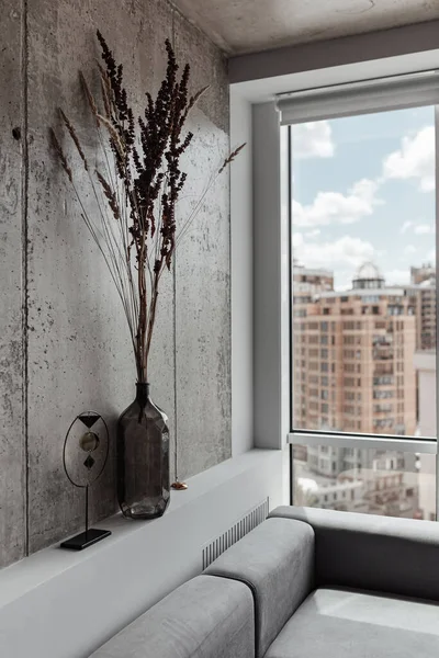 Фрагмент интерьера, вертикальная рамка с серым диваном, ваза с сухими цветами и тростник возле большого панорамного окна с видом на город — стоковое фото