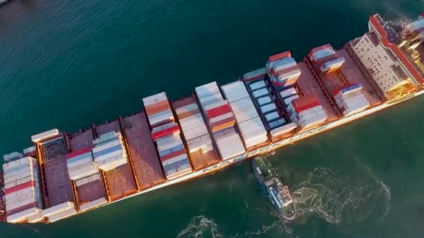 Een kleine sleepboot duwt een groot zeeschip met containers die spiraalvormige golven creëren. Bovenaanzicht naar de oceaan — Stockvideo