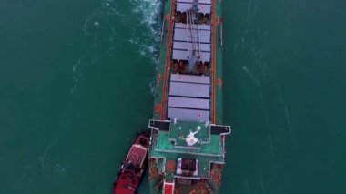 19.0da kırmızı römorkörler okyanusun dikişlerinde helikopter pisti olan büyük yeşil bir gemiyi itiyorlar. Üst görünüm