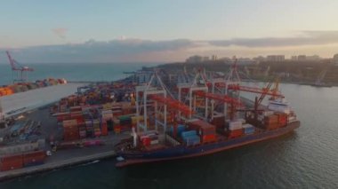 Limanın limandaki panoramik görüntüsü. Römorkör kargo gemisini kıyıya demirlemiş. Bir sürü çalışan rıhtım var. Gün batımında en üst görünüm
