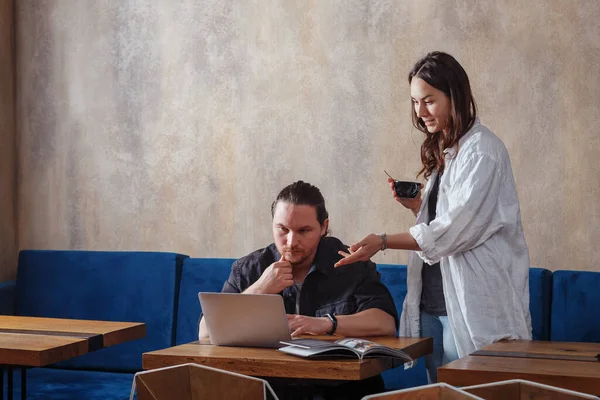 Serious couple using a laptop to read and discuss morning news or work online with a cup of coffee in a cafe, talking to a young family, making plans to search for information on the Internet on a — Stock Photo, Image