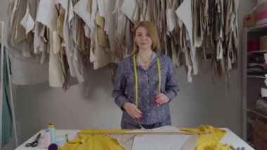 Mutlu genç bayan moda tasarımcısının portresi atölyede tek başına kameraya bakıyor. Küçük işletme sahibi ve başarılı gençlik konsepti. İpliği, çizimleri, kumaşı ve...