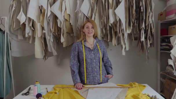 Retrato de la joven diseñadora de moda feliz sonriendo de pie en el taller solo mirando a la cámara. Propietario de una pequeña empresa y exitoso concepto juvenil. Usted puede ver el hilo, bocetos, la tela y — Vídeos de Stock