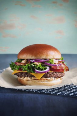 Pastırmalı hamburger, et, soğan sosu, parşömen üzerinde otlar ve domates.