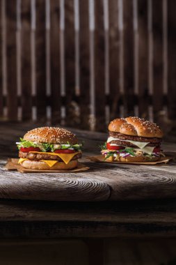İki hamburger, susamlı çörek, et, peynir, ahşap bir masada sos ve parşömen.