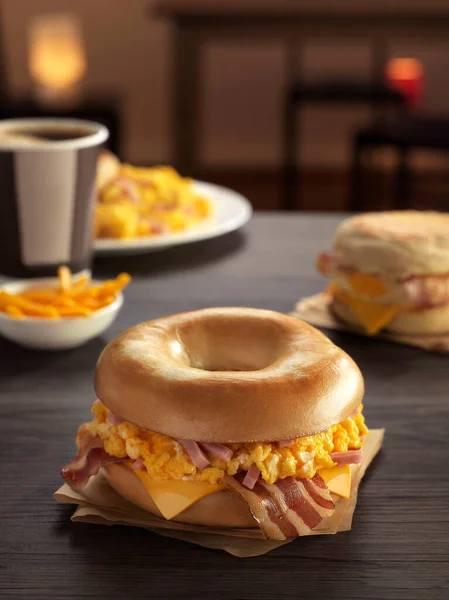 Omletli simit, kızarmış jambon, yanında patates kızartması, kahve ve kafedeki ahşap masada bir tabak omlet.