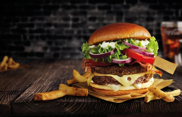 Duble etli burger, peynir ve patates kızartması ahşap bir masada, bayraklı.
