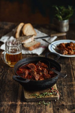 Eski bir köy masasında baharatlı et ve et kazanı içindeki ulusal yemek, dilimlenmiş ekmek.