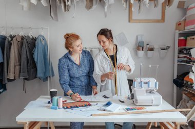 Moda tasarımcısı asistanıyla kumaş dikiyor