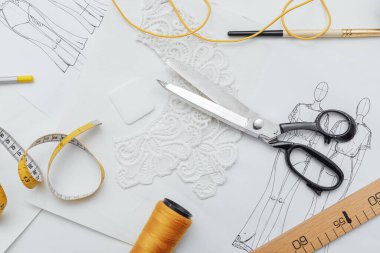 Terzinin aletleri masaya serilmiş, makas ve santimetre, çizimler ve iplikler sarı ve beyaz