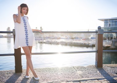 Woman leaning on railing next to water wearing summer dress