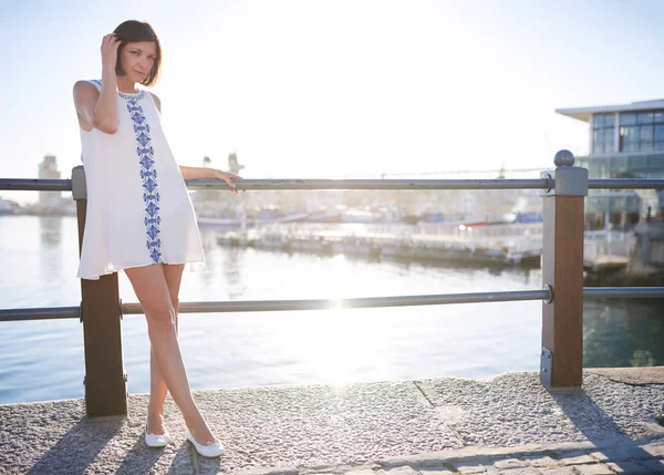 Woman leaning on railing next to water wearing summer dress