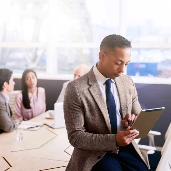 Businessman using a tablet with three colleagues seated behind him — Stock fotografie