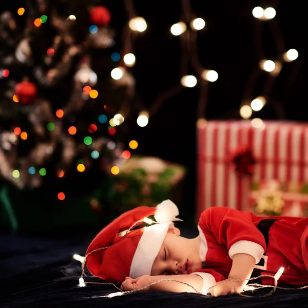 Baby sleeping in santa costume with christmas decorations as bokeh — Stock Photo, Image