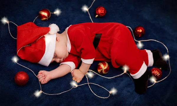 Overhead of baby sleeping in santa outfit with fairy lights — Stock Photo, Image