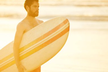 Yakışıklı sörfçü kumsalda kolunun altında bir surfboard holding