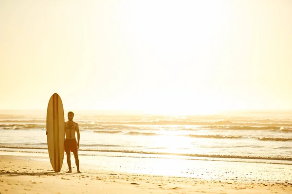 Surfer standing with his surfboard upright beside him on beach