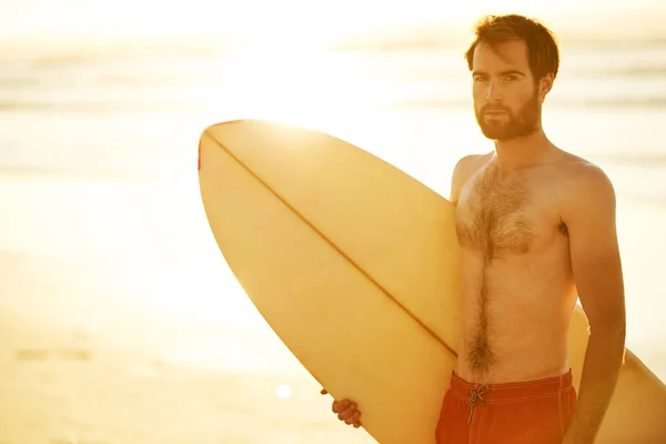 Handsome surfer holding a surfboard under his arm on beach
