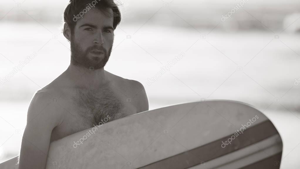 Black and white image of male surfer and retro surfboard