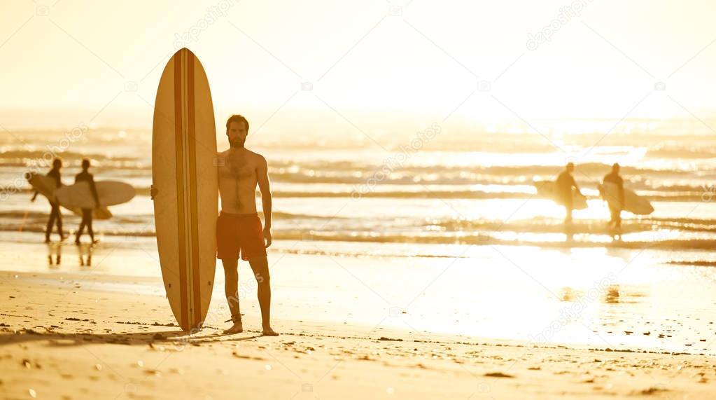 Surfer standing on beach with other surfers behind him