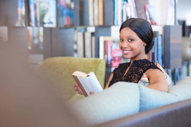 Afrikalı-Amerikalı kadın kitap okurken kameraya gülümseyen