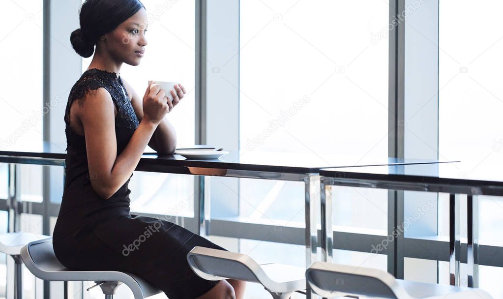 black woman sitting on bar chair next to large window
