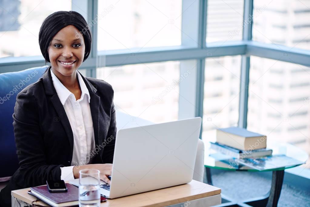Black businesswoman busy smiling at the camera seated behind computer
