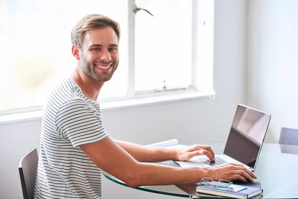 Stilig ung manlig student som ler mot kameran sitter bakom laptop — Stockfoto