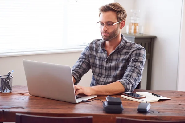 Hombre moderno escribiendo en un ordenador portátil mientras está sentado en el escritorio —  Fotos de Stock