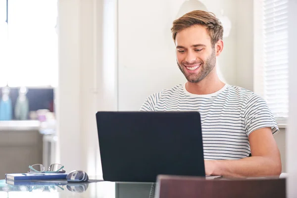 Homem atraente sorrindo para sua tela de laptop sentado em casa — Fotografia de Stock