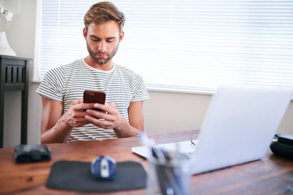 Young caucasian guy using phone while sitting at his desk — Stock Photo, Image