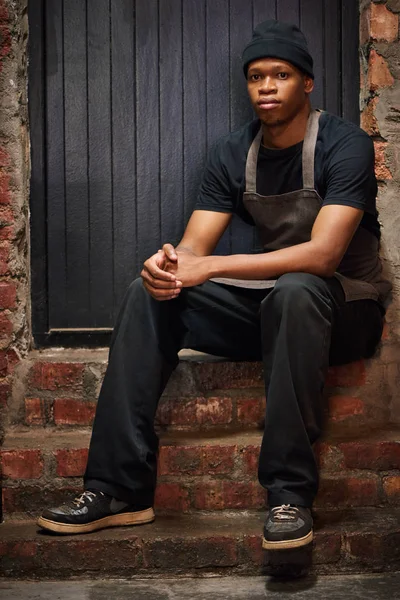 Retrato de barista preto sentado em um ambiente ligeiramente grungy — Fotografia de Stock