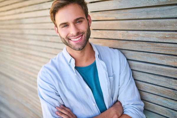 Attractive white guy smiling at camera leaning against wooden cladding — Stock Photo, Image