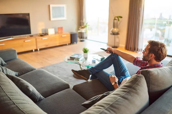 Молодой человек смотрит телевизор и переключает каналы в гостиной — стоковое фото