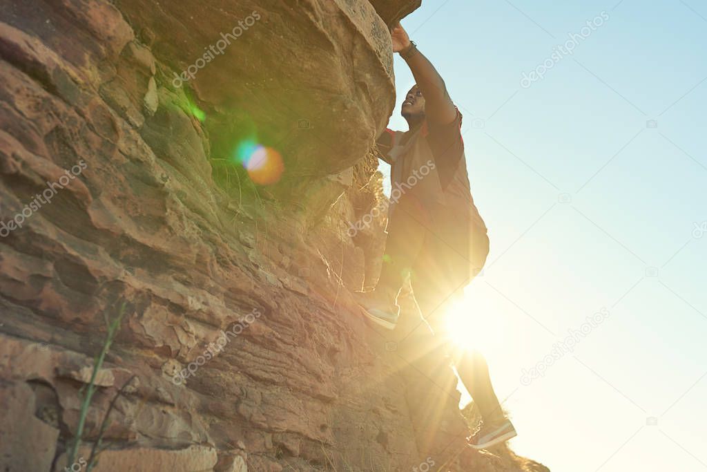 African guy climbing near vertical mountain with flare from sun