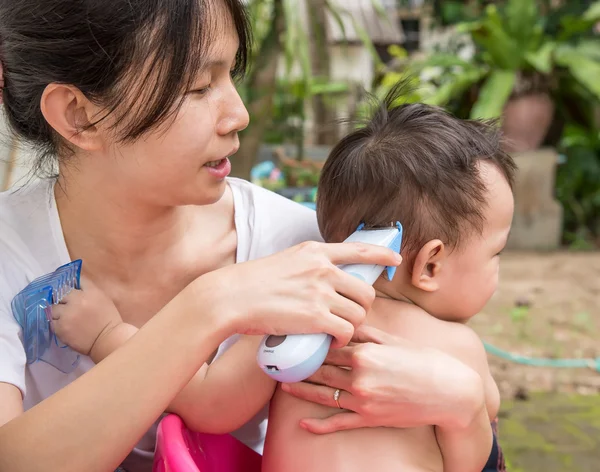 Mother cutting baby hair by hair clipper