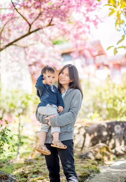 Asiatico madre holding bambino in il fioritura ciliegio fiore — Foto Stock